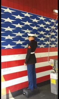 A man in uniform saluting an American flag painted on a wall inside Best Transmission in Jacksonville, FL